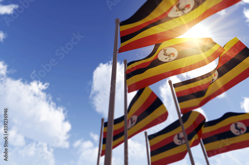 Uganda flags waving in the wind against a blue sky. 3D Rendering