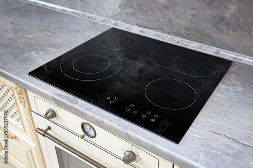 Modern kitchen interior with black induction or electric hob stove cooker with ceramic top surface with marble countertop and wall decorated with stone.