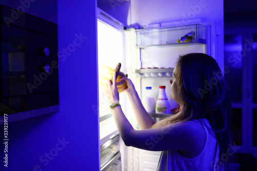 Woman at night opened refrigerator and takes out food portrait