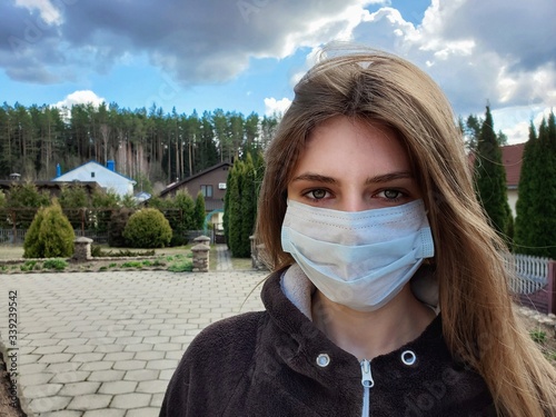 Young woman in protective sterile medical mask on her face looking at camera outdoors. Air pollution, virus, COVID-19 coronavirus quarantine concept.