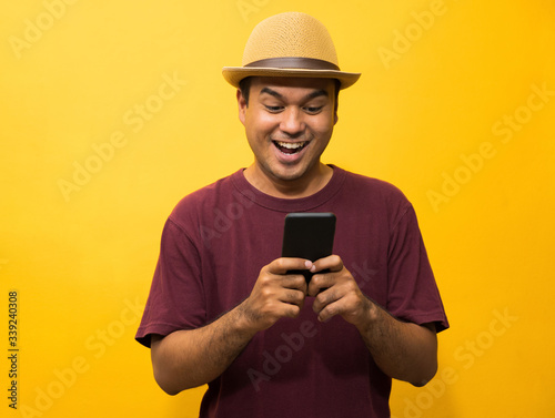 Asian man happy with his smartphone on yellow background. young man using looking at smartphone. © Nopphon