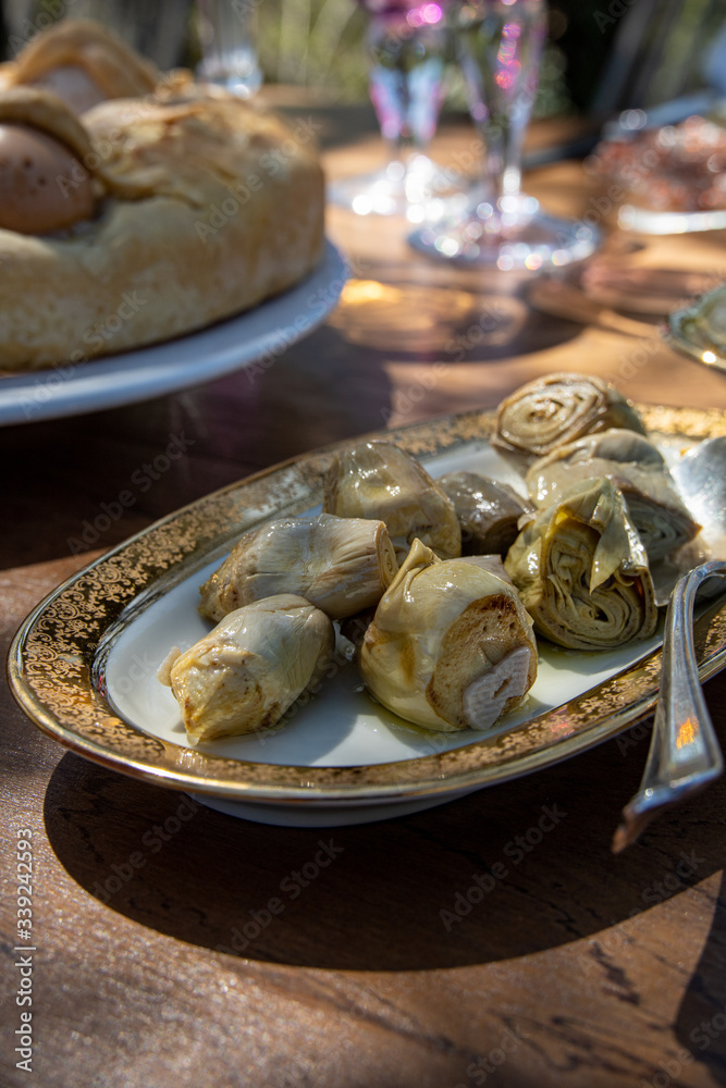 Cold appetizer of an italian typical Easter lunch: artichoke hearts preserved in oil, served in an oval vintage dish with golden decorations. Blurry background. Cold appetizer of an italian typical Easter lunch: artichoke hearts preserved in oil, served in an oval vintage dish with golden decorations. Blurry background.