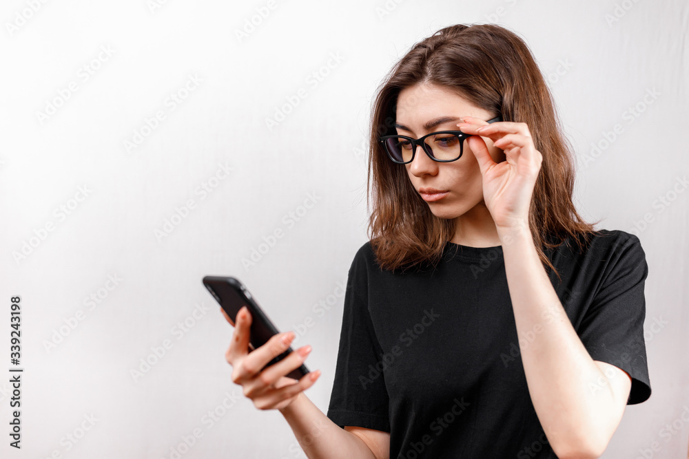 beautiful young woman on a white background looks at the phone with glasses and a black shirt. copyspace. beautiful young woman on a white background looks at the phone with glasses and a black shirt. copyspace.