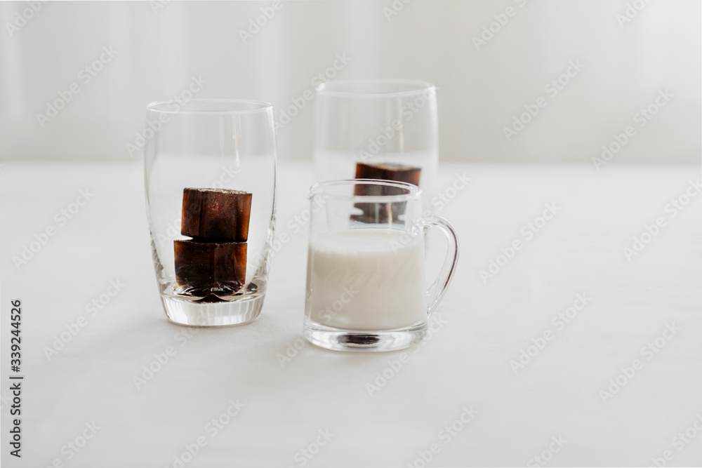 Frozen coffee ice cubes in a glass with milk to make a refreshing summer iced coffee drink. White background, isolated, copy space. Frozen coffee ice cubes in a glass with milk to make a refreshing summer iced coffee drink. White background, isolated, copy space.