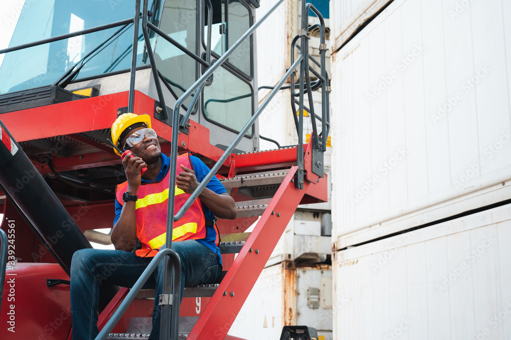 Black foreman worker working control the crane and forklift at Container cargo harbor to loading containers. African dock male staff with radio for Logistics import export shipping concept. Black foreman worker working control the crane and forklift at Container cargo harbor to loading containers. African dock male staff with radio for Logistics import export shipping concept.