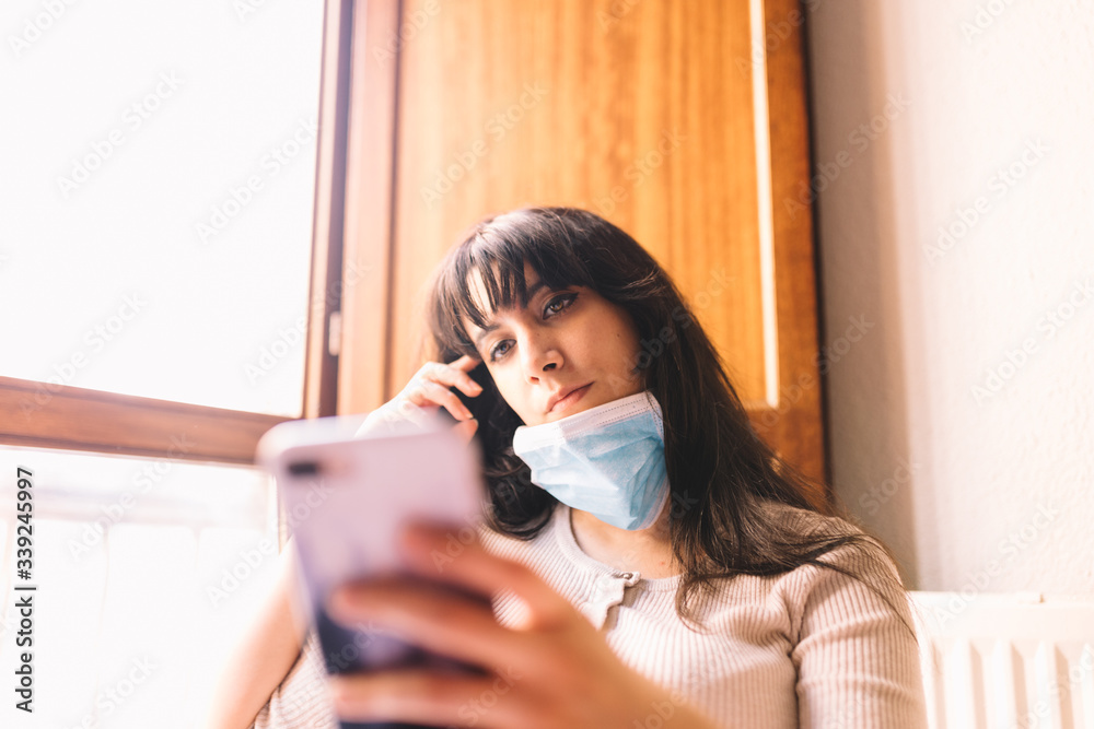 Lonely woman at home in breathing medical respiratory mask on her face using mobile phone. Chinese pandemic coronavirus, virus covid-19. Quarantine, prevent infection concept. Focus on her face. Lonely woman at home in breathing medical respiratory mask on her face using mobile phone. Chinese pandemic coronavirus, virus covid-19. Quarantine, prevent infection concept. Focus on her face.