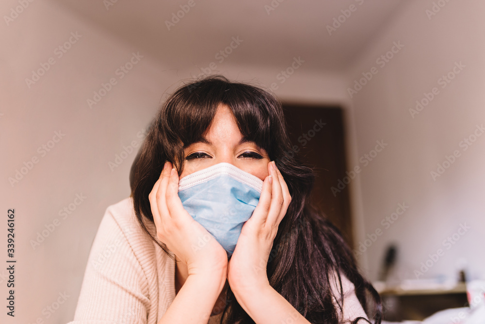 Woman at home in breathing medical respiratory mask on her face smiling hopefully. Chinese pandemic coronavirus, virus covid-19. Quarantine, prevent infection concept. Woman at home in breathing medical respiratory mask on her face smiling hopefully. Chinese pandemic coronavirus, virus covid-19. Quarantine, prevent infection concept.