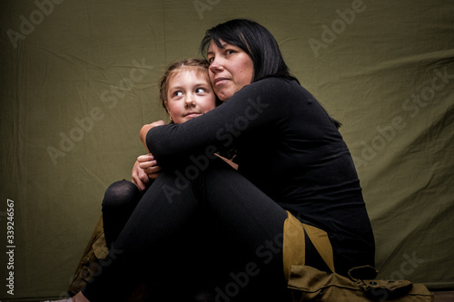 Fotografi Mother and daughter in black clothes hug sitting on a green background