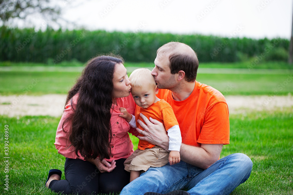 Portrait of happy parents kissing their baby son outdoors