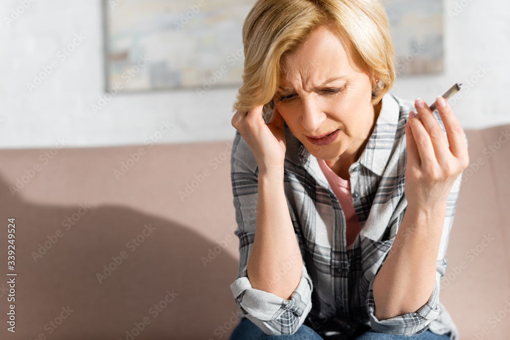 mature woman with migraine holding joint with weed at home