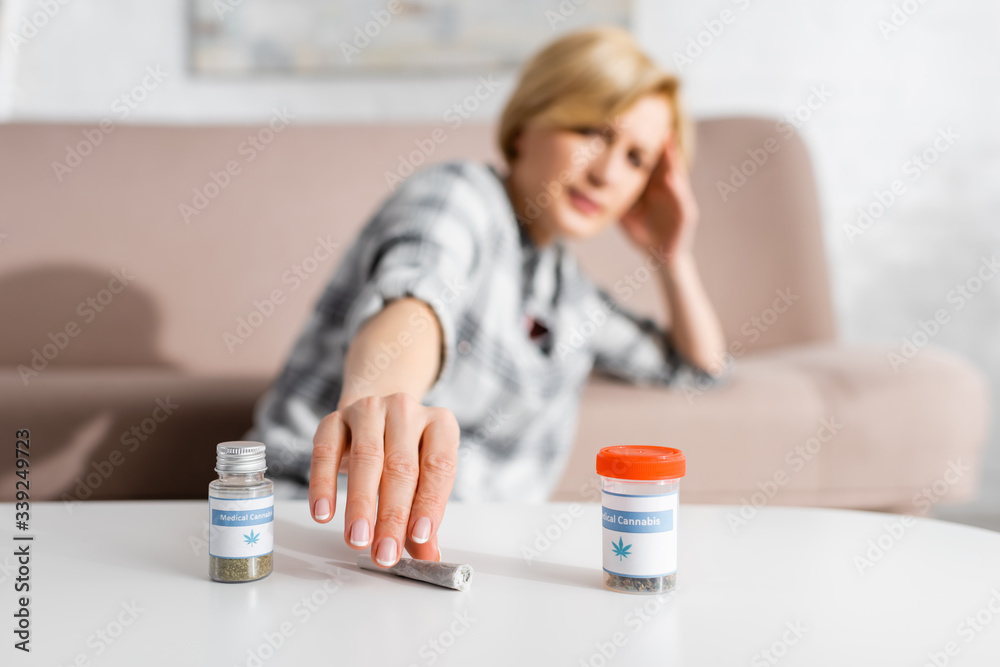 selective focus mature woman taking rolled joint with legal marijuana near bottles with medical cannabis lettering selective focus mature woman taking rolled joint with legal marijuana near bottles with medical cannabis lettering
