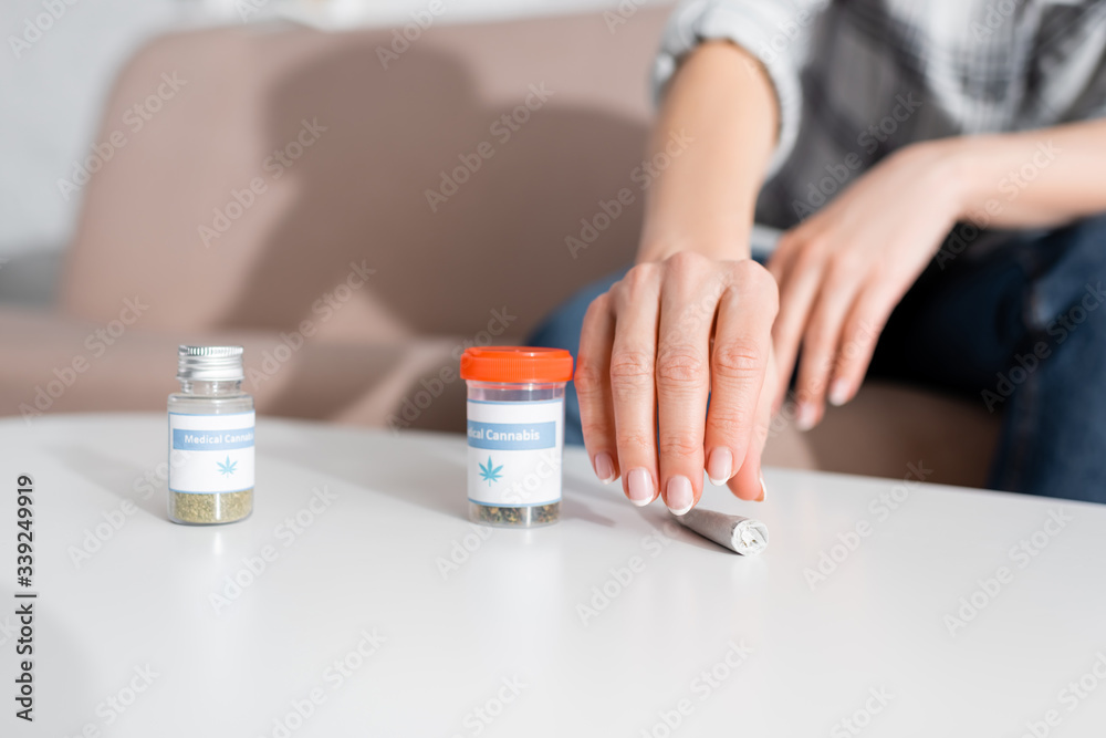 cropped view of mature woman taking rolled joint with dried marijuana near bottles with medical cannabis lettering cropped view of mature woman taking rolled joint with dried marijuana near bottles with medical cannabis lettering