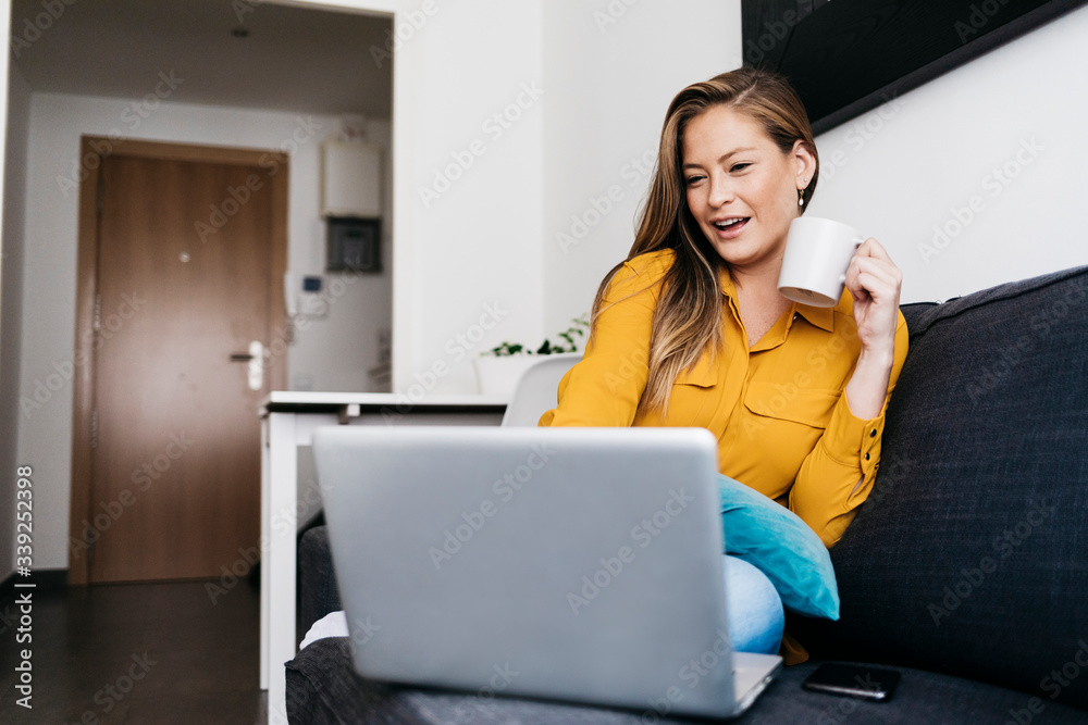 Pretty long haired female sitting on sofa with portable computer working remotely from home. Pretty long haired female sitting on sofa with portable computer working remotely from home.