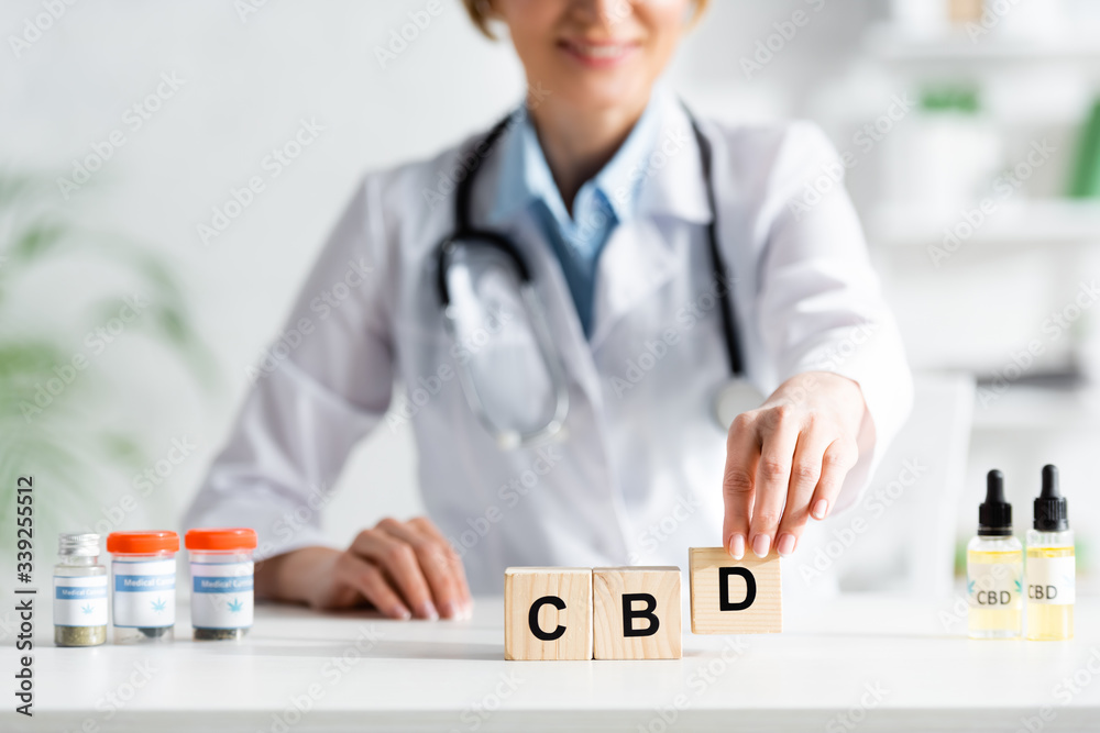 cropped view of happy doctor in white coat touching cubes with cbd lettering near drugs cropped view of happy doctor in white coat touching cubes with cbd lettering near drugs