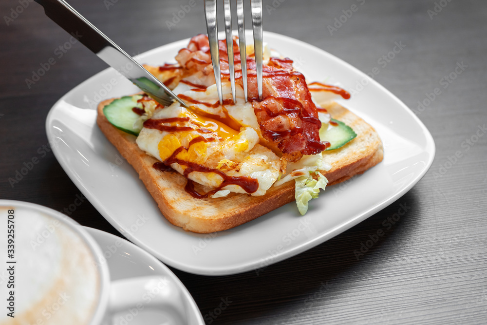 An egg and bacon sandwich is cut with a knife and fork. An egg and bacon sandwich is cut with a knife and fork.
