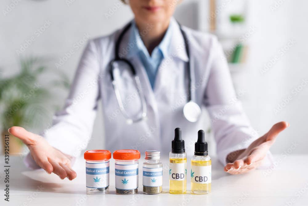 cropped view of doctor pointing with hands at bottles with cbd and medical cannabis lettering