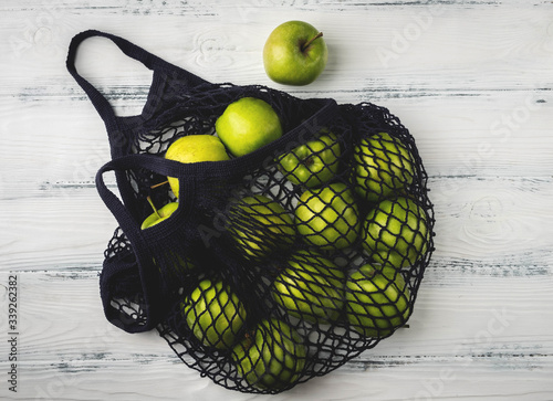 green apples in a mesh bag on a wooden background, concept of using a reusable bag without plastic