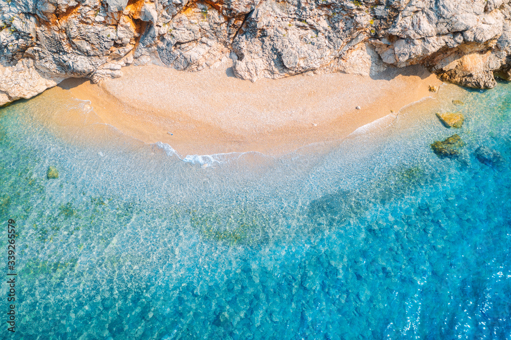 Aerial view of sandy beach with rocks and sea with transparent blue water at sunset. Coast of adriatic sea at sunset in summer. Top view. Landscape with clear azure water, waves, stones. Nature