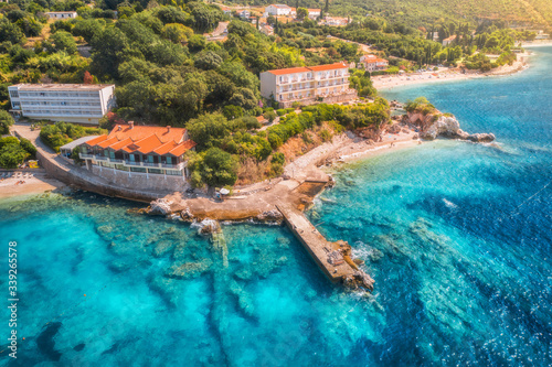 Aerial view with beautiful sea coast, sandy beach, clear blue water, hotels and green trees at sunset. Summer tropical landscape. Top view of blue sea, buildings, rocks and forest. Luxury resort