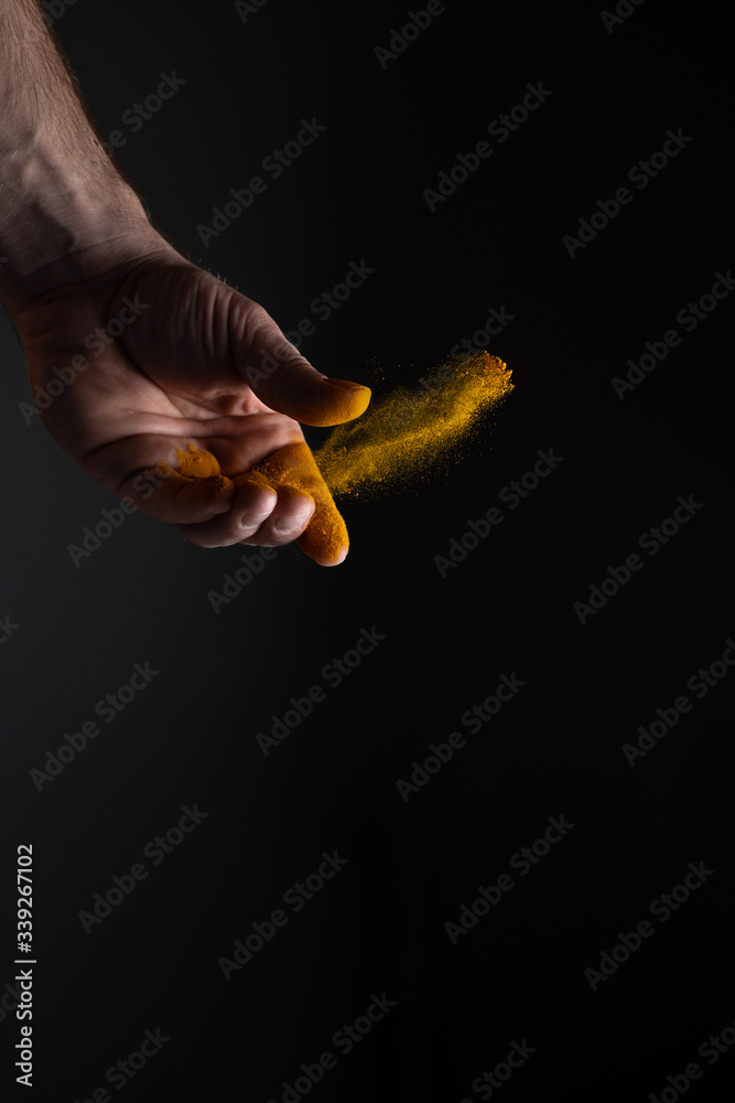 A man's hand scattering yellow colour turmeric dust which is famous eastern seasoning on black background with strong light A man's hand scattering yellow colour turmeric dust which is famous eastern seasoning on black background with strong light