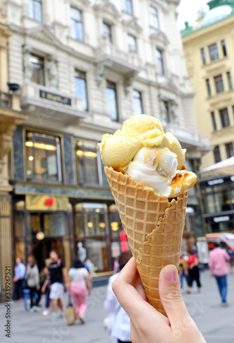 Ice cream cone in hand, on a blurred background of a crowded street in Vienna