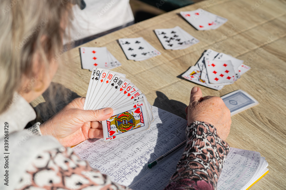 Obraz premium We are never too old to play cards. Playing cards is our common hobby. Grandmother playing cards. Grandmather's hand hold the cards. Notebook with game results.