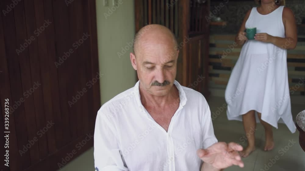 Happy mature retired couple, wife brings her husband a сup of tea and they cheerful look at the smartphone screen together at home Happy mature retired couple, wife brings her husband a сup of tea and they cheerful look at the smartphone screen together at home