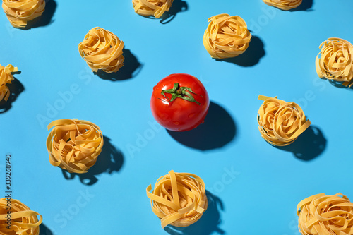 Uncooked pasta pattern and fresh red cherry tomatoes on blue background. Colorful background top view