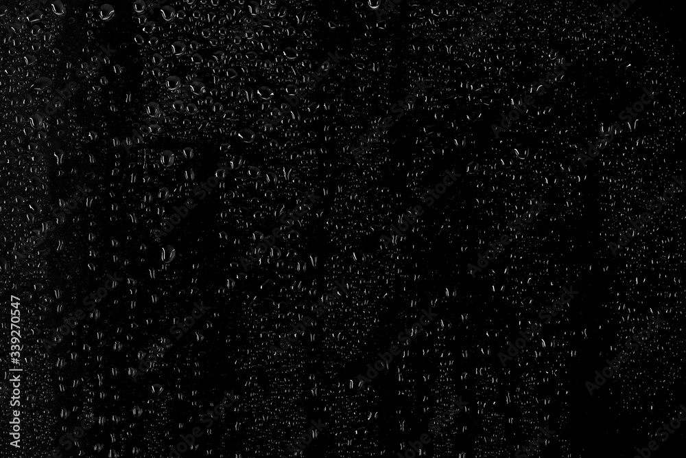 Obraz premium Drops of water flow down the surface of the clear glass on a black background. 