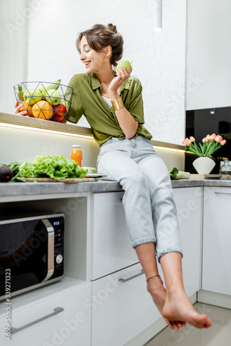 Full length portrait of a young and cheerful woman with healthy raw food on the kitchen at home. Vegetarianism, wellbeing and healthy lifestyle concept