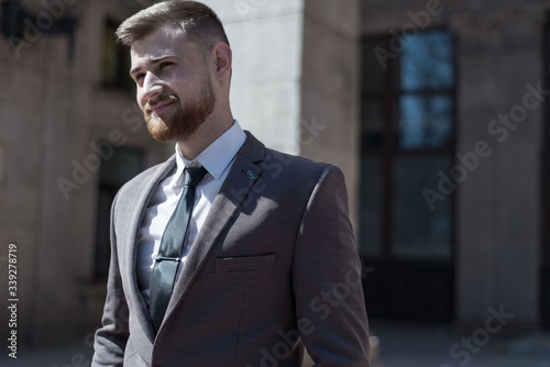 Portrait of a young bearded guy of twenty-five years old, in a business suit, against the background of an office building. Posing looking at the camera. Outdoors