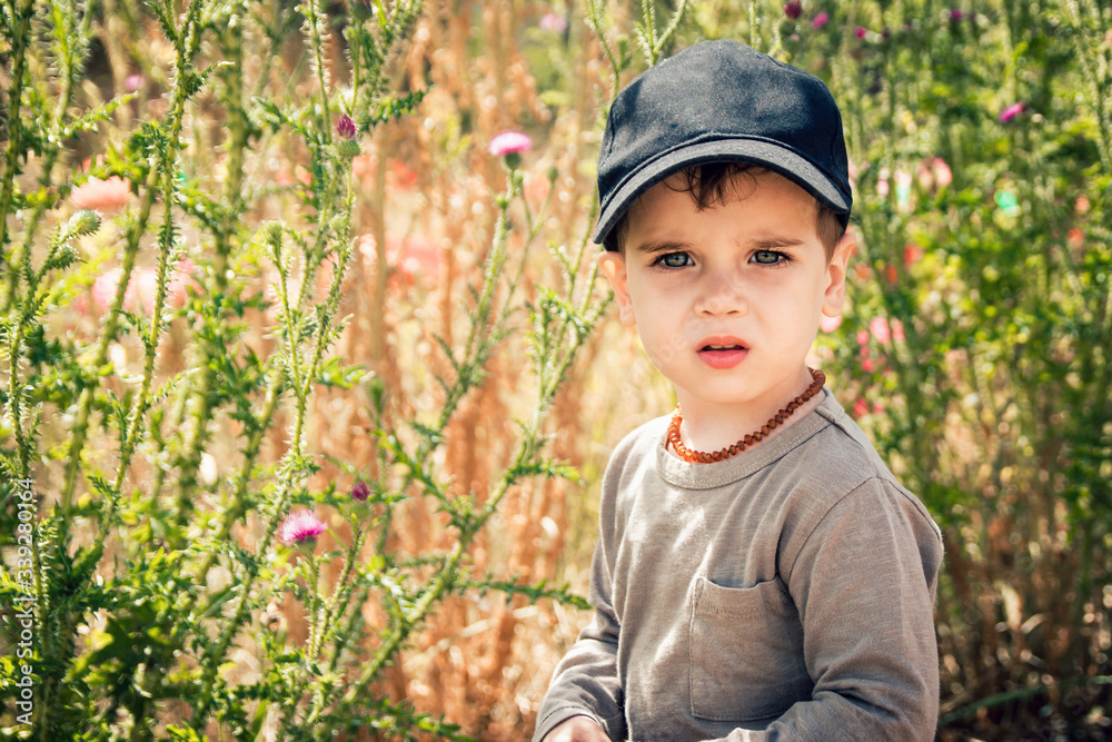 Cute toddler boy in black baseball cap and amber necklace on his neck outdoor Cute toddler boy in black baseball cap and amber necklace on his neck outdoor