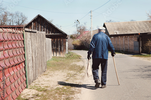 Old man in protective mask, gloves, in old clothes, with eco bag and wand walks along village road to home. Concept of old quarantined people, prevention COVID-19, Coronavirus outbreak situation