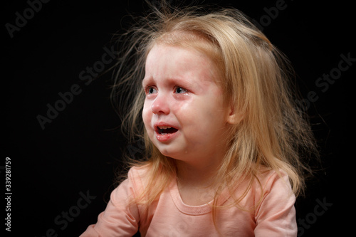 Little baby girl screaming and keeping mouth open. Close-up emotional portrait of caucasian baby girl. Funny cute child on black background.