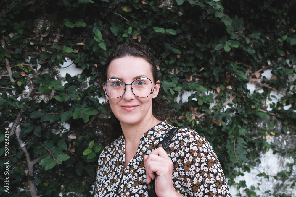 Portrait of smiling woman with funny glasses standing near the white wall with a lot of climbing plants. Portrait of smiling woman with funny glasses standing near the white wall with a lot of climbing plants.