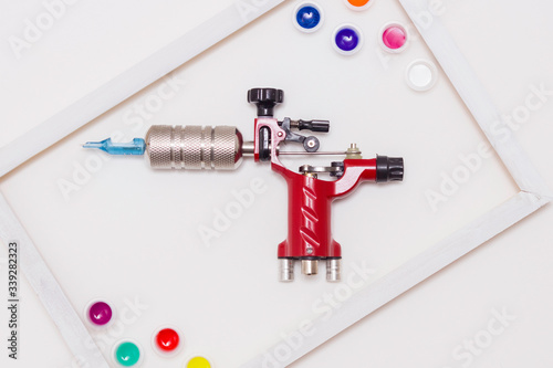 Tattoo machine on a white background, white frame, colored tattoo ink in plastic jars. The view from the top.