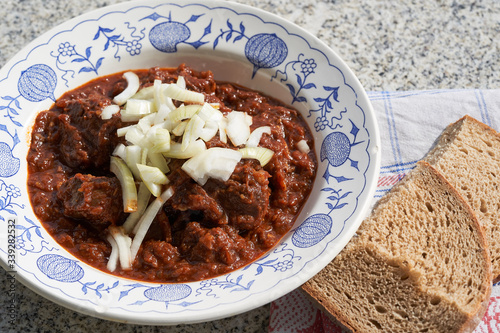 Close up Picture of Czech style beef goulash served in rustic deep plate with chopped onion on the top and slice of traditional bread. Made from slow cooked beef with sweet pepper. Traditional dish. photo