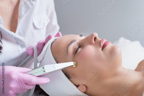 The doctor-cosmetologist makes the procedure treatment of Couperose of the facial skin of a beautiful, young woman in a beauty salon.Cosmetology and professional skin care. photo
