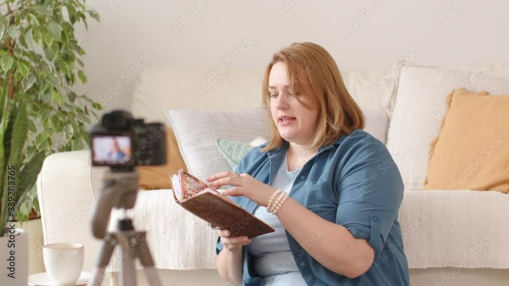 A Young Female Vlogger Recording a Video for an Online Blog with Camera on Tripod. The Blogger Talks and Gestures. Cozy White Home Interior with House Plants. Concept of Video Blogging. A Young Female Vlogger Recording a Video for an Online Blog with Camera on Tripod. The Blogger Talks and Gestures. Cozy White Home Interior with House Plants. Concept of Video Blogging.