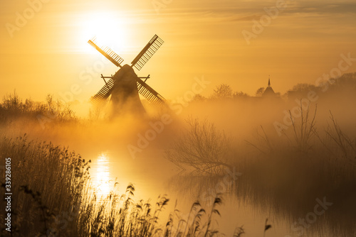 Yellow sunrise with traditional, Dutch windmill and a canal in the spring fog.