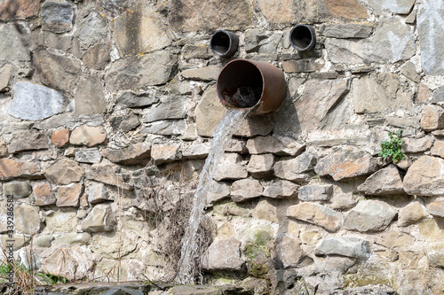 Three old pipes with flowing water on a stone wall. direction of water flow in the right direction. city drainage system. water pollution