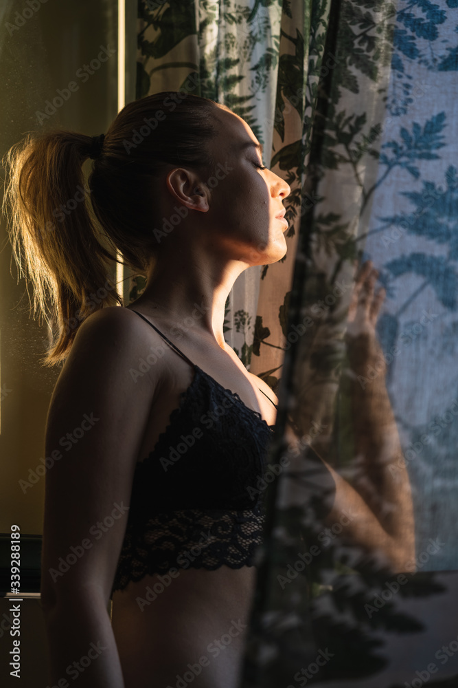 Obraz premium Young woman looking through curtains.