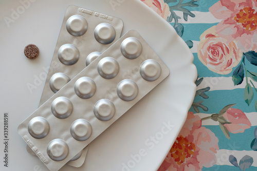 Iron pills on a plate. Many tablets of Ferrous sulfate. Supplement use for Iron Deficiency Anemia. Floral retro background. Pastel color.
