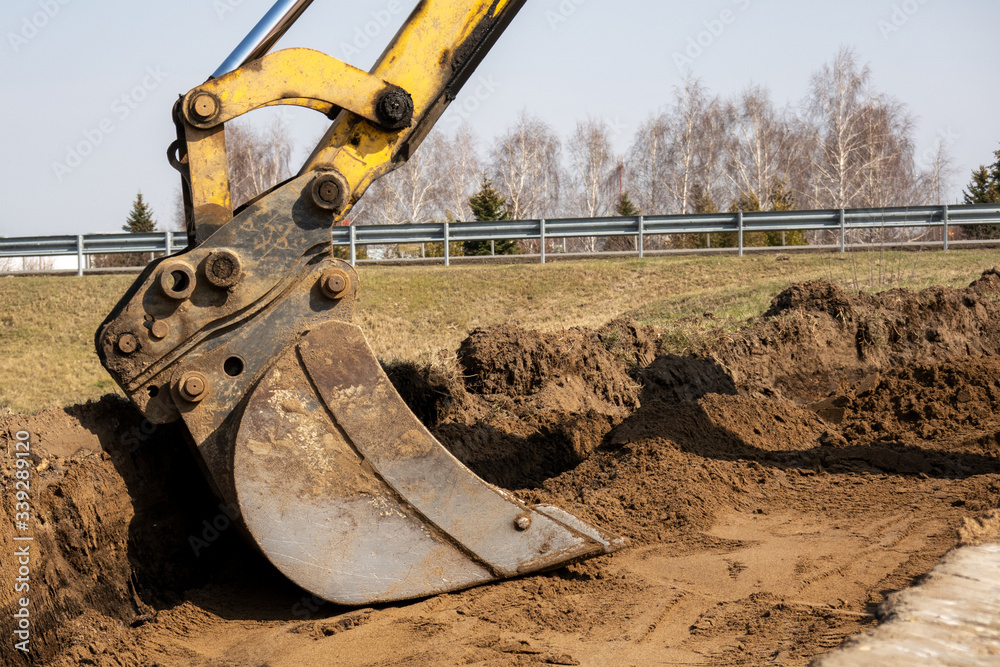 Fototapeta premium Road repairs. Expansion of the roadbed. Bucket excavator close-up rakes the soil.