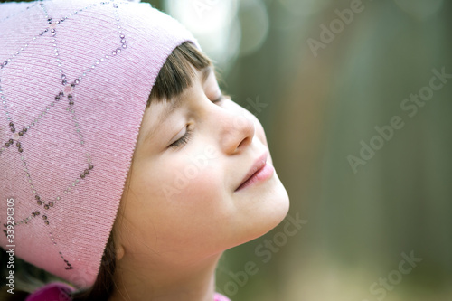 Portrait of young pretty child girl wearing pink jacket and cap enjoying warm sunny day in early spring outdoors.