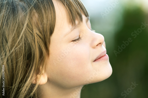 Portrait of young pretty child girl with long hair enjoying warm sunny day in summer outdoors. Cute female kid relaxing on fresh air outside.
