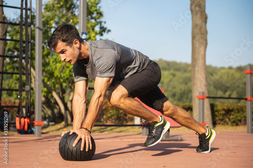 Fit guy doing exercises using a ball outdoors. Young athletic man training in city park