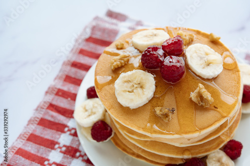 breakfast, pancakes with raspberry, nuts, banana and honey on a white plate