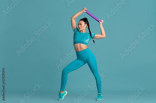 Upper body. Beautiful young female athlete practicing in studio, monochrome blue portrait. Sportive fit brunette model with elastics. Body building, healthy lifestyle, beauty and action concept.