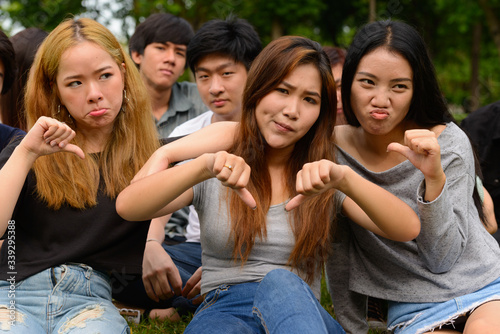 Stressed young group of friends giving thumbs down together at the park